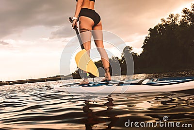 partial view of tattooed girl standing on sup board on river Stock Photo