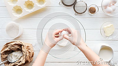 Partial view of woman cracking egg in bowl while cooking on table. Stock Photo