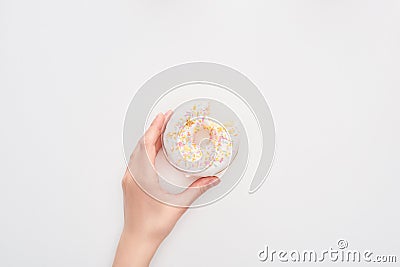 Partial view of woman holding glazed bitten white doughnut with sprinkles on white background. Stock Photo