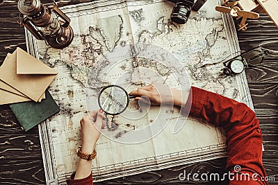 partial view of woman with magnifying glass looking for destination on map on wooden tabletop with photo camera, compass Stock Photo