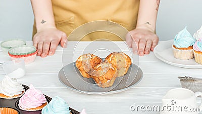 Partial view of woman near table with plate with cupcakes isolated on grey. Stock Photo