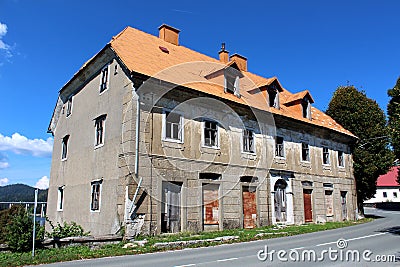 Partially destroyed abandoned large family house with broken windows and rusted rollup blinds on doors mounted on dilapidated Stock Photo