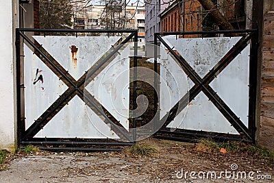 Partially rusted open heavy metal doors with black frame and sheet metal fillings preventing access to abandoned backyard Stock Photo