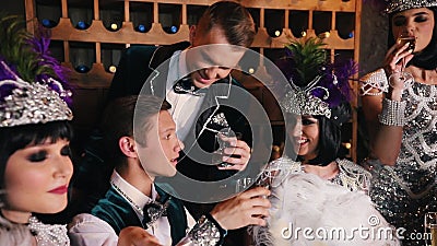 Partie de thème - les jeunes dans de rétros vêtements de scintillement se reposant derrière la table et l'alcool potable banque de vidéos Partie de thème - les jeunes dans de rétros vêtements de scintillement se reposant derrière la table et l'alcool potable banque de vidéos