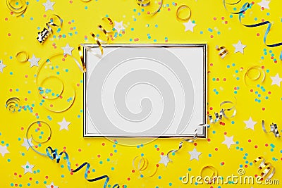 Party, carnival or birthday background decorated silver frame with colorful confetti and streamer on yellow table top view. Stock Photo