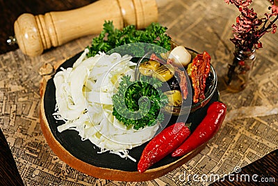 Bar snacks portion on wooden board: cecil cheese, hot peppers, olives, sun-dried tomatoes, fresh parsley leaves. Stock Photo