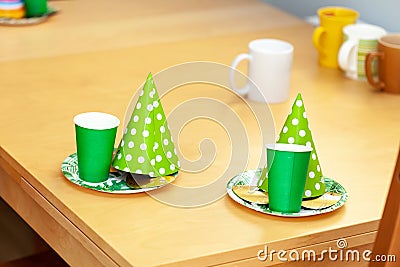 Party hats, paper plates, masks and green cups laying on the table ready for a kids birthday party, two sets, objects, closeup Stock Photo