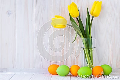 Paschal greeting card, mockup with text space. Festive easter frame with colorful eggs and bouquet of yellow tulips on light wood Stock Photo