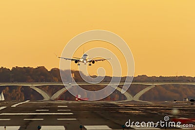 A passenger airline is slowly descending to land on a runway at sunset. Stock Photo