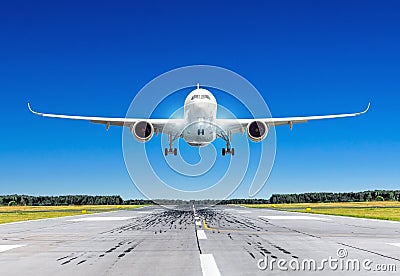 Passenger airplane with bright landing lights landing at in good clear weather with a blue sky on a runway. Stock Photo