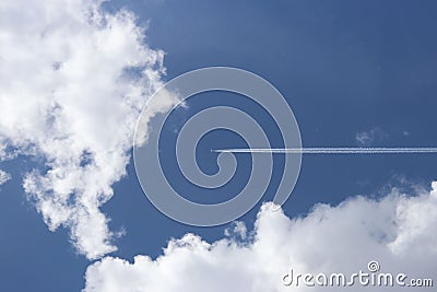 A passenger airplane flying high in the sky among the clouds. Air liner leaving a trace of exhaust gases glowing in the sun. Ecolo Stock Photo