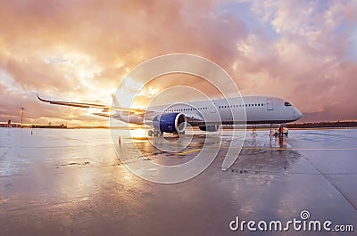 Passenger commercial wide-body aircraft parked with a wet apron at the airport during evening rain at sunset with beautiful sky Stock Photo