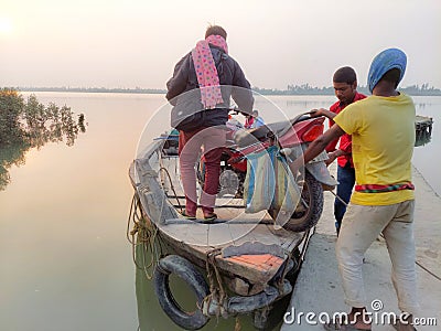 A passenger with his motorcycle keeping on boat with the help of boat men to cross matla river at sundarban. Editorial Stock Photo