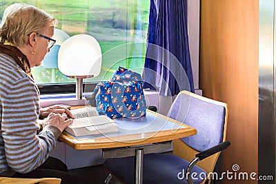 A passenger reading a book sitting at the dining car of a Greek Editorial Stock Photo