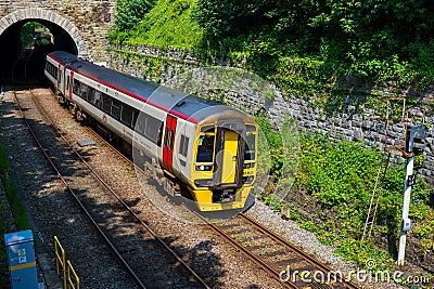 Passenger train emerging from a tunnel surrounded by greenery and stone walls on a sunny day Editorial Stock Photo