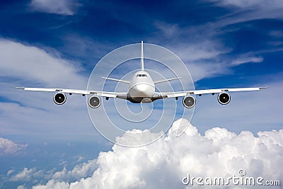 The passenger wide body plane flies high in the blue sky above clouds. Airplane closeup front view Stock Photo