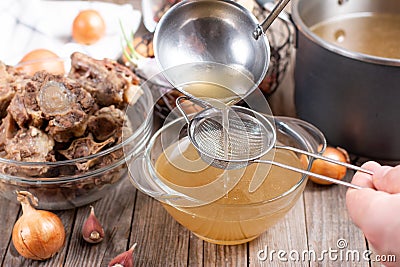 Passing the bone broth through a sieve. Concentrated Bone Broth in a bowl on the table Stock Photo