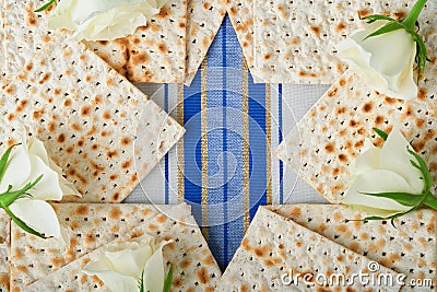 Passover celebration concept. Blue Star of David made from matzah, white and yellow roses, kippah and walnut on bluebackground. Stock Photo