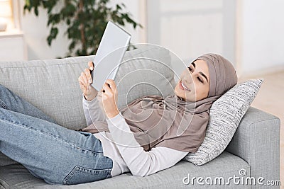 Passtime At Home. Relaxed Muslim Girl Lying On Couch With Digital Tablet Stock Photo