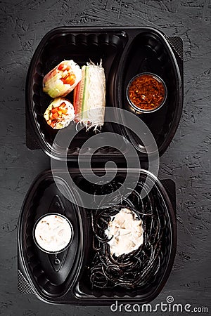 Pasta with cuttlefish ink and rolls of rice paper with vegetables in eco boxes. on a black background Stock Photo