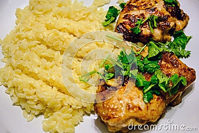 Pasta Orzo with grilled chicken. Macaroni in the form of rice with meat and herbs. Pasta on a plate with fried chicken sprinkled Stock Photo