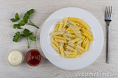 Pasta in plate, parsley, mayonnaise and ketchup, fork on table Stock Photo