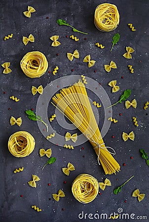 Pasta in the shape of a butterfly, spiral, nests and spaghetti, red and black peppercorns, salt on a dark background Stock Photo