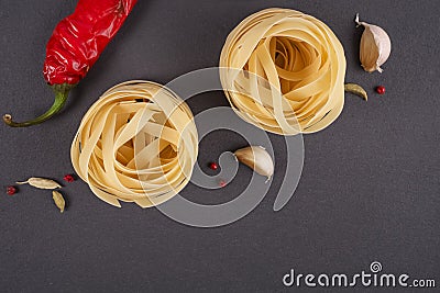 Pasta Top view. Two Fettuccine nest on a gray background with spices. Hot peppers, fennel seeds and chilli peppers. Flat lay Stock Photo