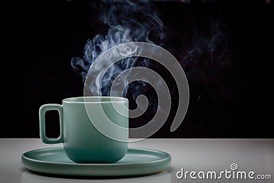 Pastel green colored coffee or tea cup with hot liquid, smoke and steam, black background Stock Photo