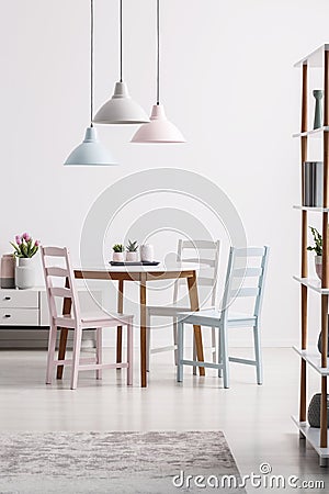 Pastel lamps above table with chairs in white dining room interior with grey carpet. Real photo Stock Photo