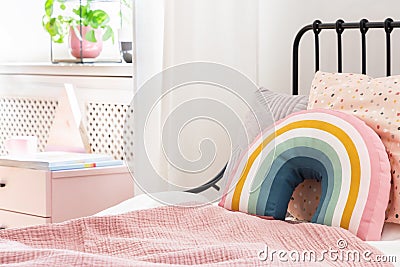 Pastel pillows on pink bed in girl`s rainbow bedroom interior with white cabinet. Stock Photo