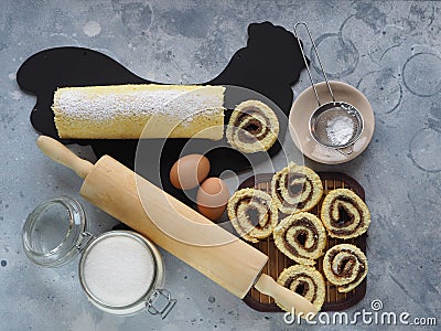 Pastry background.Homemade roll with plum jam, sprinkled with powdered sugar, on a black chopping Board in the shape of a rooster Stock Photo