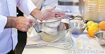 Pastry chef Baker sieving flour into a bowl in the kitchen of the bakery Stock Photo