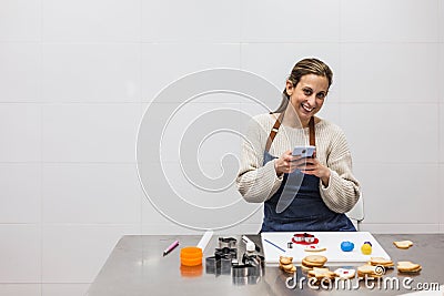 Pastry chef taking picture with phone of cookies while looking at camera Stock Photo