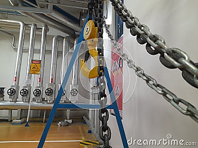 Pasuruan, 27 April 2022 : Industrial chain crane hooks hanging with sash in factory isolated against white wall background Editorial Stock Photo