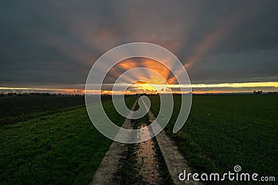 Sunbeams shine at the bottom of the clouds after sunset. A path is leading to the horizon. Stock Photo