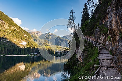 A path with a wooden fence climbs steeply beside the Braies lake Stock Photo