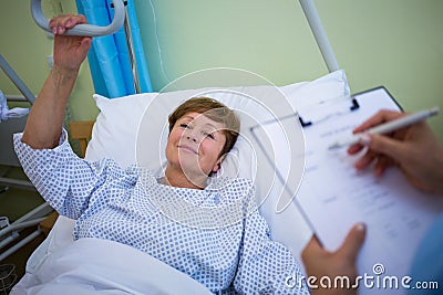 Patient lying on bed while nurse writing on clipboard Stock Photo