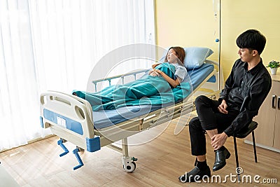 In the patient room, the young woman patient sleeps due to fatigue from the disease. With a boyfriend sitting to encourage beside Stock Photo