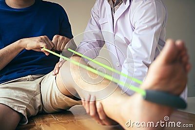 Patient use resistance band stretching out his leg with physical therapist helps in clinic room Stock Photo