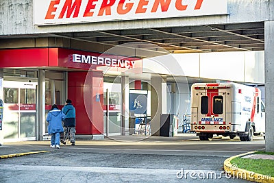 Patients go to the hospital to an emergency entrance, an ambulance and paramedics car stand nearby Editorial Stock Photo