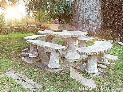 Patio with a stone bench in a seating area of a home garden with green grass and plants. Sunset time and empty copy space Stock Photo