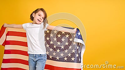 Happy child, cute girl with American flag on yellow studio background. USA celebrate July 4th, independence Day. Stock Photo