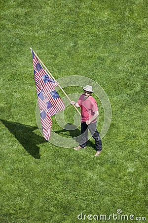A patriotic man with a US Flag made of many US Flags stands alone in a green grass lawn at an anti-Iraq War protest march in Santa Editorial Stock Photo