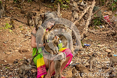 Monkeys surrounded a happy tourist who feeds them with fruit Editorial Stock Photo