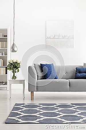 Patterned carpet in front of grey couch with blue pillows in white loft interior with flowers. Real photo Stock Photo
