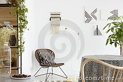 Patterned cushion on chair and plant on table in white boho living room interior with posters. Real photo Stock Photo