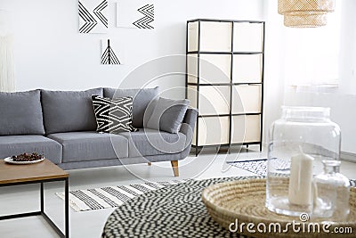 Patterned cushion on grey sofa next to screen in modern flat interior with posters. Real photo Stock Photo