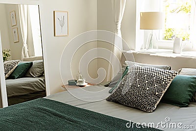 Patterned and green pillows on bed in simple bedroom interior wi Stock Photo