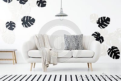 Patterned pillow and blanket on sofa in white living room interior with monstera leaves. Real photo Stock Photo